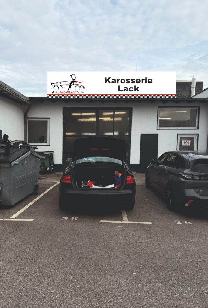 Black sedan parked by a glass building with trees and hills in the background.